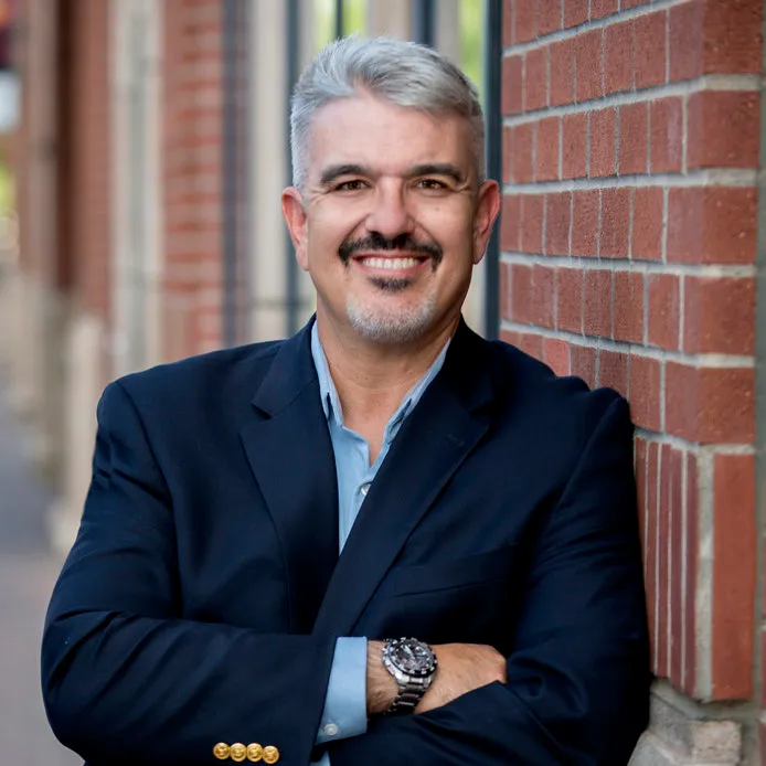 Portrait of Scott Novis in a navy blazer, leaning against a brick wall.